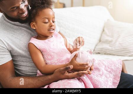 Nahaufnahme des afrikanischen Vaters, der eine kleine piggy Bank der Tochter zeigt Stockfoto