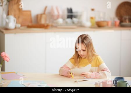 Weitwinkelporträt süßer Mädchen, die Ferienkarte für Muttertag oder Valentinstag machen, während sie am Tisch in gemütlichem Heim sitzen, Kopierer Stockfoto