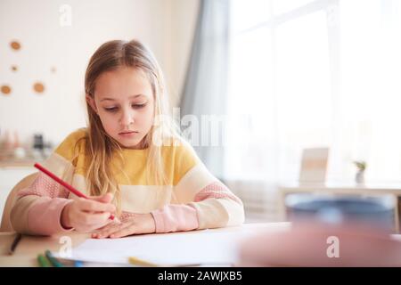 Warmes gezungtes Porträt von niedlichen kleinen Mädchen, die Bilder zeichnen oder Hausaufgaben machen, während sie am Tisch im Innenbereich sitzen, Platz kopieren Stockfoto