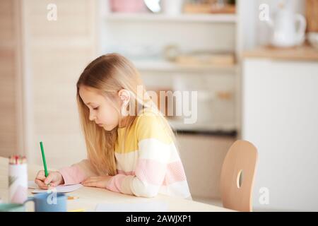 Seitenansicht Portrait von niedlichen kleinen Mädchen Zeichnen von Bildern oder Hausaufgaben machen, während sie am Tisch im Innenbereich sitzen, Kopierraum Stockfoto