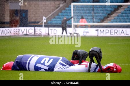 Die Mitarbeiter kämpfen bei starkem Wind vor dem Sky Bet Championship Match in Den, London, um eine Mittelkreisabdeckung zu halten. Stockfoto