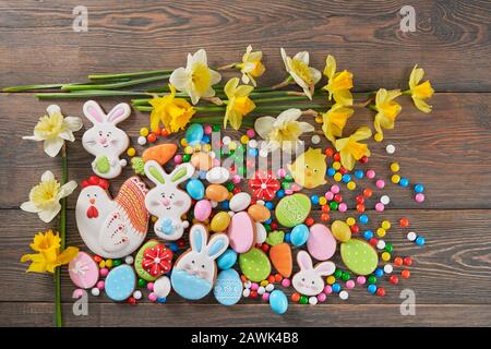 Von oben Blick auf bunte Ingwer glasierte Plätzchen und Schokoladenkugeln und Narzissen isoliert auf Holzhintergrund. Hausgemachtes köstliches Gebäck in Form von ostertieren, Eiern und roten Blumen. Stockfoto