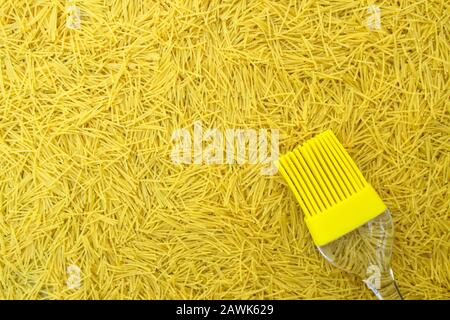 Hintergrund mit italienischer Pasta vermicelli und gelber Silikon-Küchenbürste oder Quasten mit transparentem Griff Stockfoto