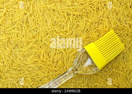 Hintergrund mit italienischer Pasta vermicelli und gelber Silikon-Küchenbürste oder Quasten mit transparentem Griff, Platz für Text- und Designelemente Stockfoto