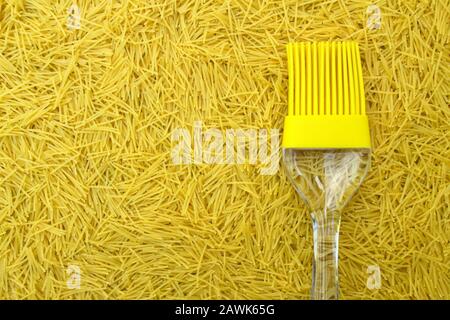 Hintergrund mit italienischer Pasta vermicelli und gelber Silikon-Küchenbürste oder Quasten mit transparentem Griff, Platz für Text- und Designmenüs oder Stockfoto