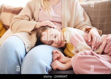 Warmtoniges Porträt eines süßen Mädchens, das auf dem Schoß der Mütter schläft, während es zu Hause auf der Couch liegt, Kopierraum Stockfoto