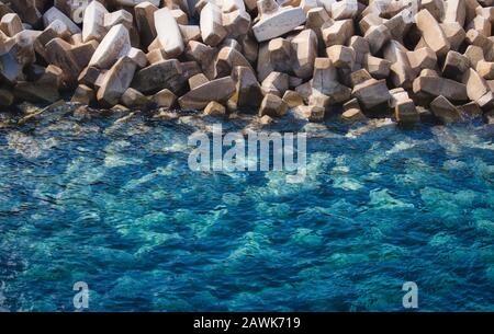 Strukturierter Hintergrund von klaren blauen Meer- und weißen Steintetrapoden zur Verhinderung von Erosion Stockfoto