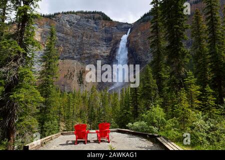 Zwei rote Stühle an einer Unterseite von Takakkaw fallen an einem sonnigen Nachmittag. Takakkaw Falls ist ein Wasserfall im Yoho-Nationalpark in der Nähe Von Field, British CA Stockfoto