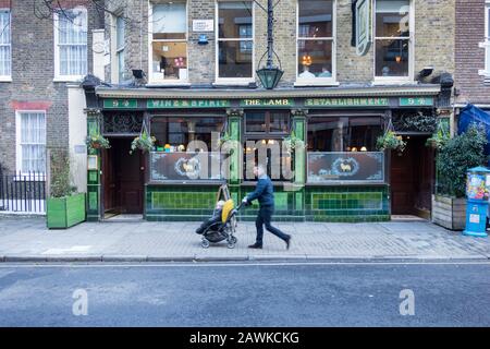 Ein Mann, der ein Kind in einem Buggy am öffentlichen Haus von Lamb (einem denkmalgeschützten Pub der Klasse II) in der Lamb's Conduit Street, Bloomsbury, London, Großbritannien, vorbeischiebt. Stockfoto