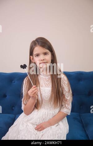 Das Mädchen sitzt auf einem blauen Sofa in einem hellen Zimmer und posiert Stockfoto