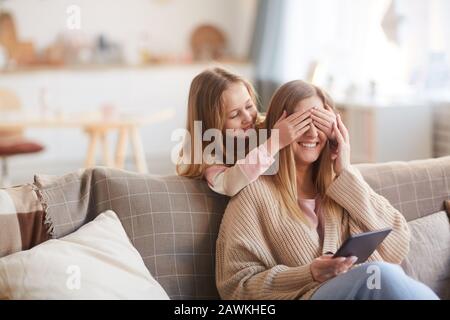 Warmer gezungter Portrait von niedlichem Mädchen, das einen Buh mit fröhlicher junger Mutter spielt, während er sie am Muttertag überraschte, kopiere Raum Stockfoto