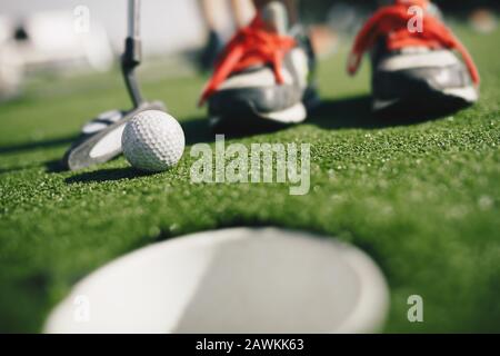 Kinder spielen Minigolf. Nahaufnahme des Spielers in den Sickern mit Minigolfclub und weißem Golfball. E-Cup im foregroundGold Hole Th Stockfoto