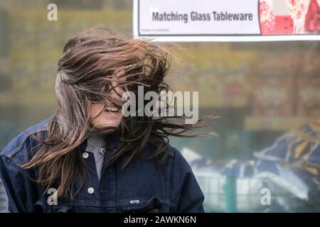 Eine Frau, die einen schlechten Haartag hat, während ihr Haar im Windwetter weht und dabei Tangles verursacht, während gale Kräftewinde durch die Straßen fegen Stockfoto