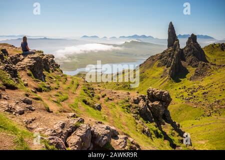 Portree, Schottland/Großbritannien - 27. Juni 2019: Eine Frau sitzt auf einer Klippe mit Blick Auf Den Alten Mann von Stoor, einen 74 m hohen Landzettel mit einem steilen, felsigen Gesicht auf einer Clou Stockfoto