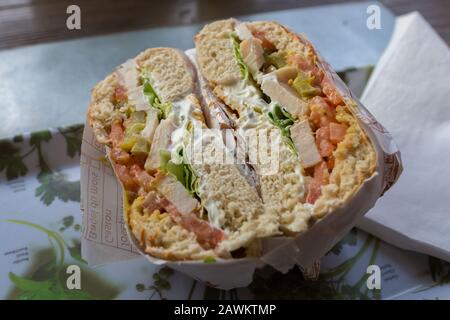 Nahaufnahme des in zwei Hälften geschnittenen Sandwiches mit Hähnchen-, Tomaten-, Salat- und Joghurt-Sauce. In Papier verpackt. Lecker und lecker. Stockfoto