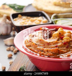 Frischer hausgemachter Hummus in Tonform mit Olivenöl, Kichererbsen, Gewürzen und sonnengetrockneten Tomaten auf Steintisch Stockfoto