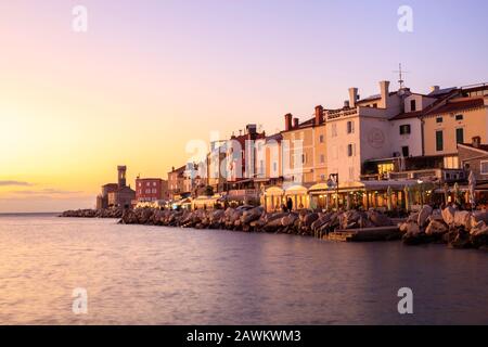 Sonnenuntergang über Piran auf der Halbinsel Istrien, Slowenien. Der Leuchtturm und die Kirche Unserer Lieben Frau von Gesundheit am Ende der Promenade. Stockfoto