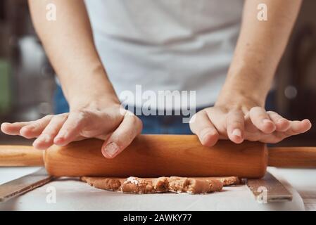 Weibliche Hände Rollenteig auf Tisch. closeup. Frau, die Teig für das Backen in der Küche Stockfoto