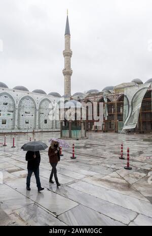 Zwei Personen, die im Regen durch den Innenhof der Sultan-Ahmed-Moschee (Blaue Moschee) spazieren, im Hintergrund sichtbare Wiederherstellungsarbeiten. Istanbul, Türkei Stockfoto