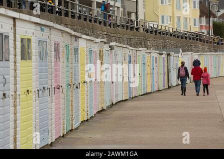 Menschen, die im Februar an Strandhütten an der Küste von Lyme Regis vorbeilaufen. Lyme Regis ist berühmt für den Cobb Harbour und das Sammeln von Fossil. Dorset Engl Stockfoto