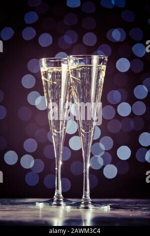 Zwei Gläser Champagner auf dunklem Bokeh-Hintergrund. Urlaubskonzept. Festlicher Bokeh-Hintergrund. Vertikaler, getonter, warmer Ton Stockfoto