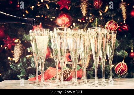 Brille für Party auffüllen. Viele Gläser Champagner mit Weihnachtsbaumhintergrund. Party-Setup. Hintergrund der Weihnachtszeit. Traditionelle rote und grüne Weihnachtsdekoration mit Lichtern. Feiertagsparty. Horizontal Stockfoto