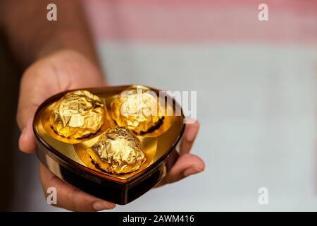 Valentines Day Geschenkhintergrund mit Kopierbereich. Junge männliche Hand hält und gibt herzförmige Luxus-Schokolade-Box. Konzept für Liebespaare, Romantik. Stockfoto
