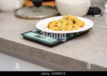 Bulgur, Weißfisch und Gemüse im Küchenmaßstab. Köstlicher, gesunder, warmer Salat auf einem Marmortisch. Bulgur pilaf. Kalorien zählen.Nahaufnahme. Stockfoto