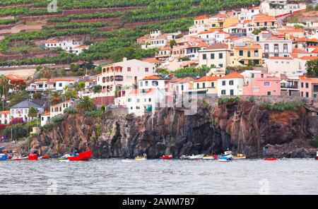 Fischerboote ankerten in der Nähe der felsigen Küste. Küstenlandschaft von Funchal, der Hauptstadt der Insel Madeira, Portugal Stockfoto