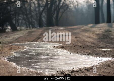 Gefrorene Pfütze am Morgen auf einer Feldstraße. Stockfoto