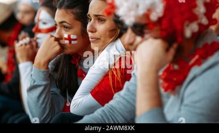 Enttäuschte Fans im Sportstadion, die das Spiel ungläubig verfolgen, während ihre Mannschaft das Spiel verliert. Verärgerte Gruppe englischer Fans, die traurig nachher schauen Stockfoto