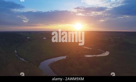 Luftbild: Flug über den Schönen Fluss und die grünen Felder. Weiches Licht bei Sonnenuntergang. Majestätische Landschaft. Stockfoto