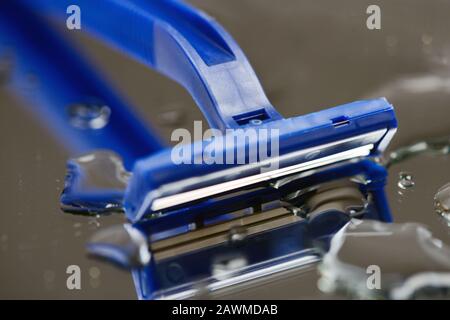 Makroansicht der Rasierklinge auf Wassertropfen Hintergrund. Rasieren Sie das Rasierklingenradar auf einer feuchten Oberfläche mit grauem Spiegel Stockfoto