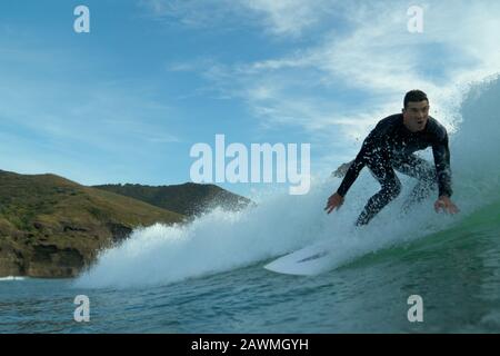 Ein junger männlicher Surfer in einem schwarzen Wetsuit reitet eine Welle am Piha Beach, Piha, West Auckland. Stockfoto