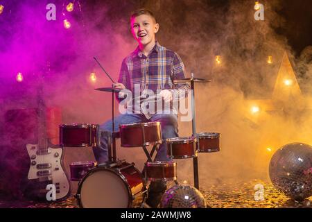 Junge, der das Schlagzeug auf schwarzem Hintergrund mit Rauch im Tonstudio oder auf der Bühne spielt. Stockfoto