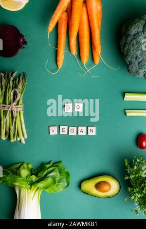 Draufsicht Satz von gesundem Rohgemüse auf grünem Hintergrund mit Go vegan Meldung auf Holzblöcken. Vegetarische und vegane Ernährung. Veganismus. Nachhaltige li Stockfoto