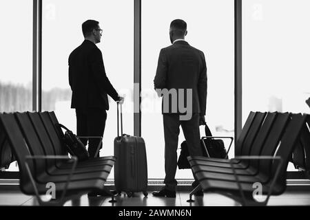 Silhouette von zwei Geschäftsleuten, die vor einem großen Fenster am Flughafen in der Nähe des Abflughters stehen. Stockfoto