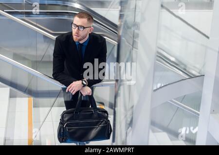 Hochwinkelige Draufsicht mit attraktivem, reifer Mann in schicker Form. Er steigt mit Telefon und Koffer in den Händen die Treppe hoch Stockfoto