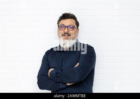 Entspannter mittelöstlicher leitender Geschäftsmann mit Brille und stilvollem Bart, der gegen die Mauer lächelt Stockfoto