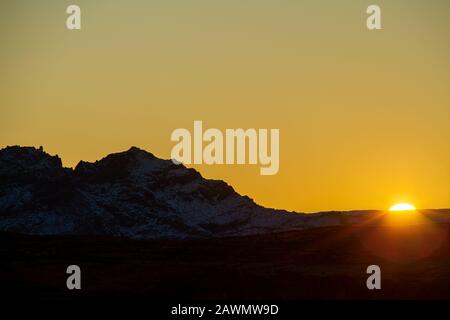 Sonne am Horizont mit einem schneebedeckten Berg in der Wüste von Arizona. Stockfoto