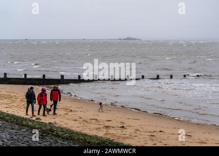 Menschen, die Hunde am Strand spazieren, während der Sturm Ciara das Wetter in Southend on Sea, Essex, Großbritannien beeinträchtigt. Die Leute haben sich gegen die Kälte gewickelt Stockfoto