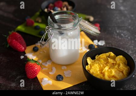 Bio-Kokosnussreis trinken mit Kokosflocken in einem konservierenden Glas mit Strohhalm und Cornflakes bei Sonnenschein Stockfoto