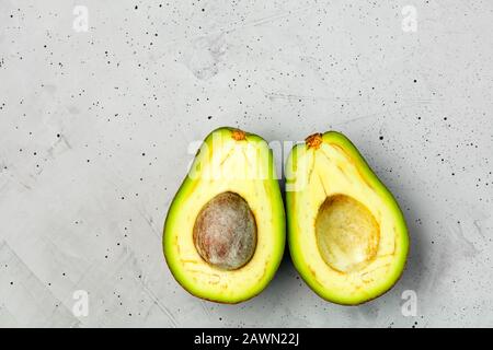 Avocado halbiert, eine Scheibe mit Kern auf grauem Betonhintergrund, Nahaufnahme. Köstliche und nahrhafte Früchte, Bild mit Kopierraum. Stockfoto