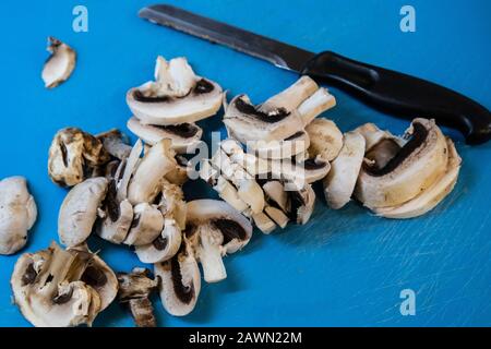 Gehackte gemeine Pilze Agaricus bisporus und ein Küchenmesser auf einem Schneidebrett, bevor sie zur Zubereitung von Speisen verwendet werden. Stockfoto