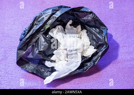 Eine schwarze Plastiktüte mit verschraubten gebrauchten Geweben und leeren Tablettenpackungen Stockfoto