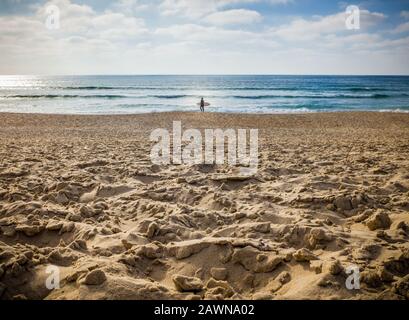 Einsame Person, die am Strand mit einem Surfbrett läuft Ein sonniger Tag Stockfoto