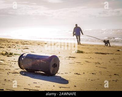 Alte rostige Fass links am Strand mit einer Person Und ein Hund im Hintergrund Stockfoto