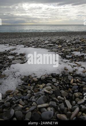 Vertikale Aufnahme von auftauendem Schnee auf den Kieselsteinen auf dem Strand Stockfoto