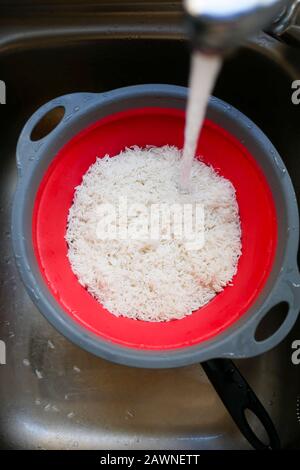 Bereiten Sie Reis zum Kochen vor, indem Sie ihn durch Wasser in einem Sieb waschen. Stockfoto