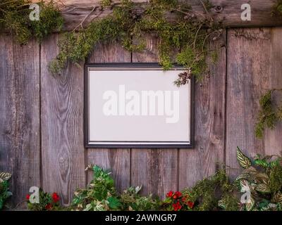 Leeres Whiteboard auf einem Holzzaun, umgeben von Pflanzen und Blumen Stockfoto